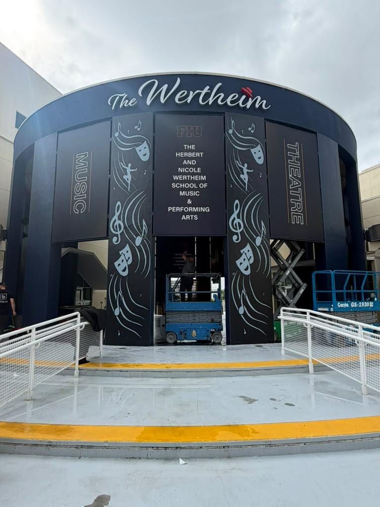 Entrance to the FIU Wertheim School of Music and Performing Arts clad in dark panels with white music and theater illustrations, a scissor lift inside during install