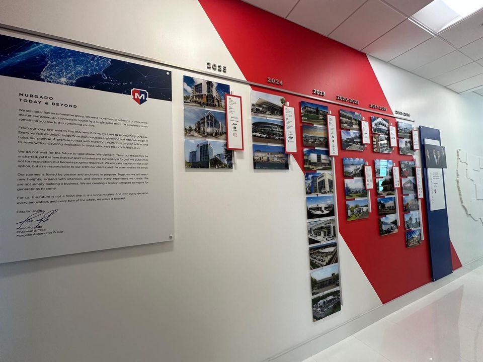 Murgado Automotive Group corridor wall with a 'Murgado Today and Beyond' letter panel beside a red and white timeline of dealership photos grouped by year