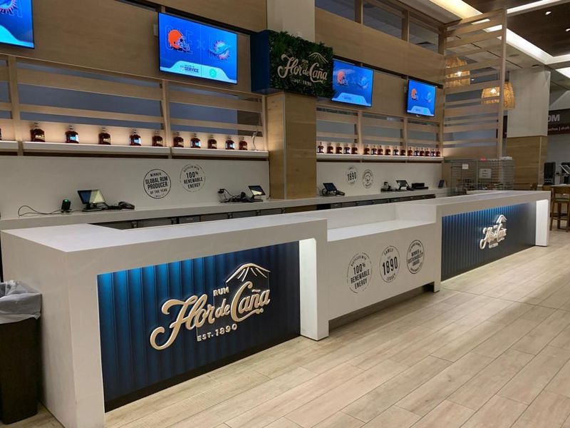 Illuminated Flor de Cana branded bar front and back-bar graphics installed on a concourse at Hard Rock Stadium