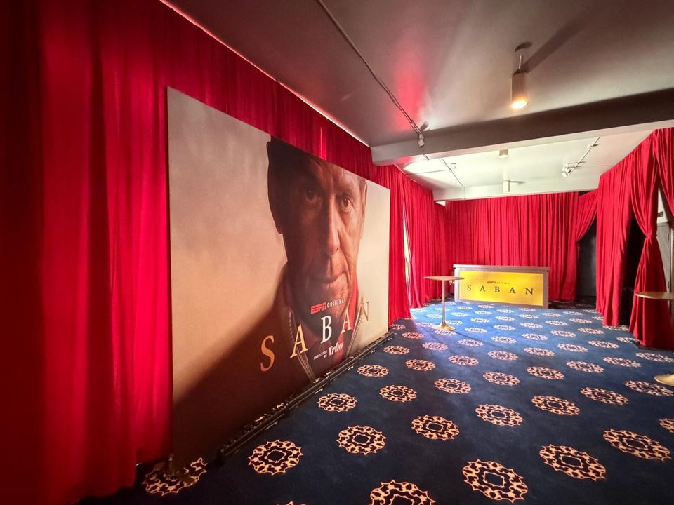 Oversized ESPN Original Saban portrait backdrop along a red-draped event room, with a gold branded bar counter at the far end