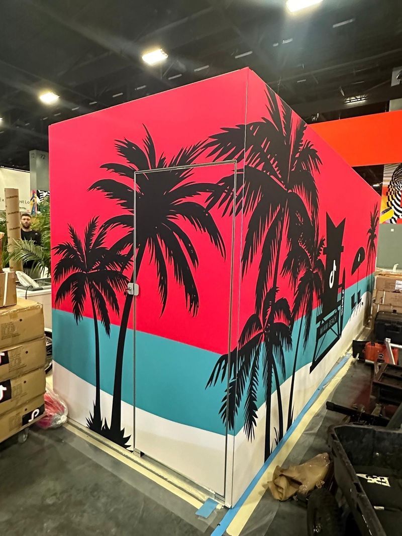 Pink and turquoise TikTok exhibit wall graphics continuing across a door, with black palm-tree silhouettes