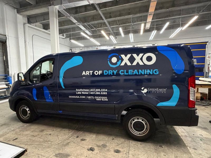 OXXO dry-cleaning delivery van wrapped in navy and blue graphics with a large white logo and contact details