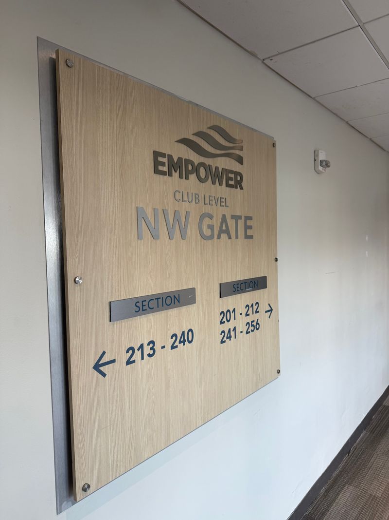 Wall-mounted sign reading Empower Club Level NW Gate with section number ranges and directional arrows