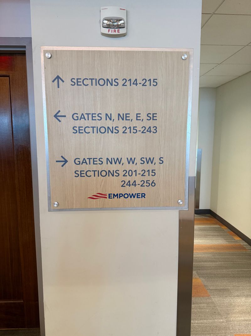 Wood-grain directional wall sign with arrows for stadium section and gate numbers, Empower logo at the base